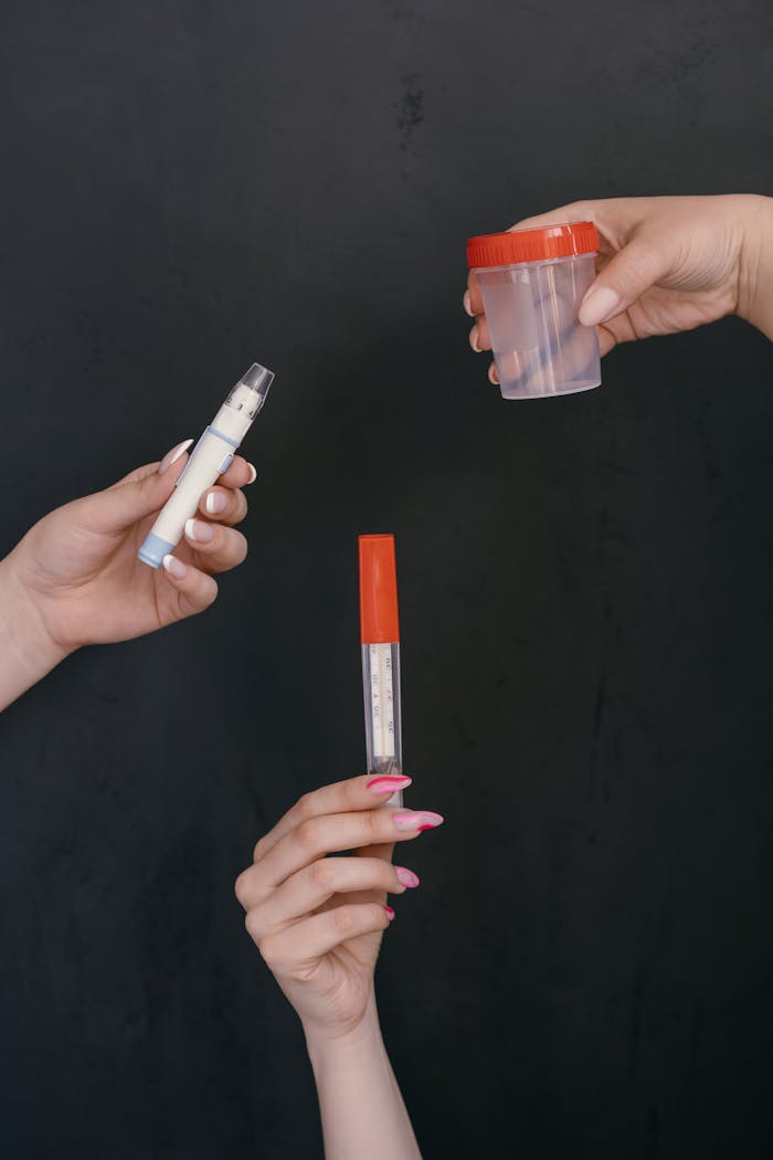Three hands holding medical items including thermometer and sample container against dark backdrop.